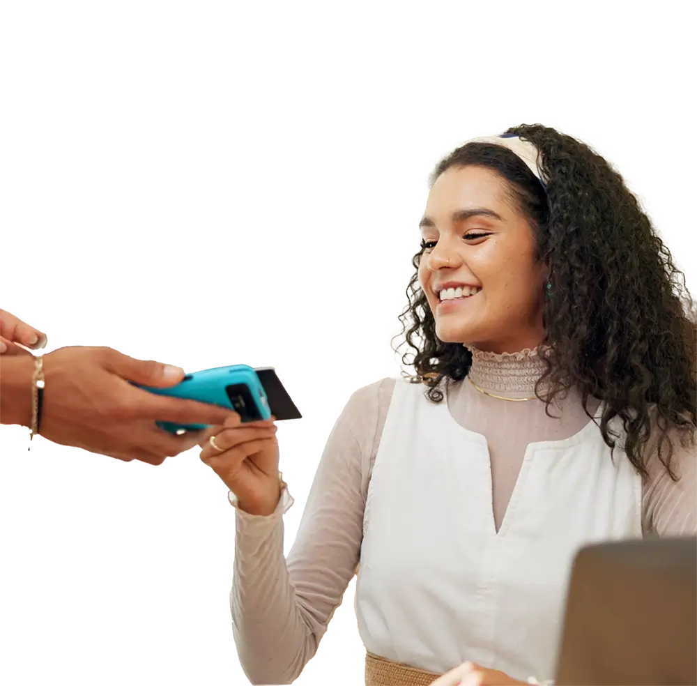 An African American young woman with curly hair holding a credit card over a credit card reader at a restaurant and smiling, depicting credit card processing